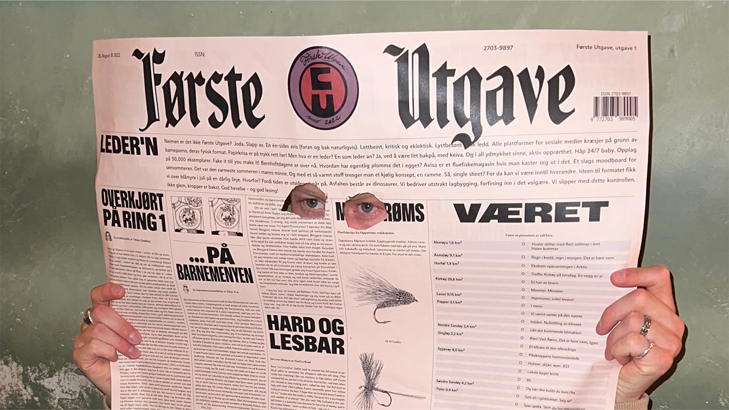 A person holding up the A1 format newspaper «Første utgave» with holes cut out for eyes